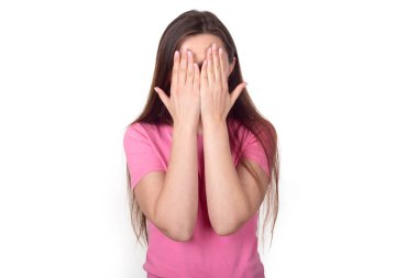Şok oldum. Elleriyle yüzünü örten pembe kazaklı esmer kadın, beyaz arka planda izole edilmiş. Metin için yer.