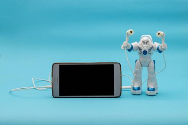 Mavi arka planda kulaklığı ve akıllı telefonu olan oyuncak astronot. Reklam için kavram, metin için yer.