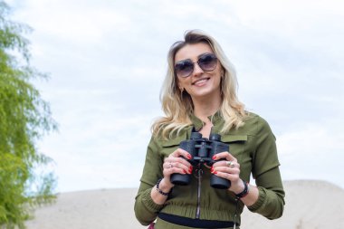 Dürbünlü ve gözlüklü güzel bir kadın doğanın arka planına bakar..