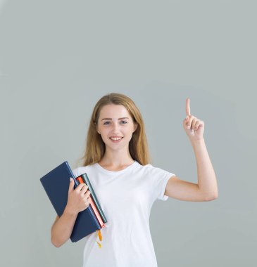 Kitapları yukarı gösteren ve gri arka planda kameraya bakan bir kadın öğrenci. Metin için yer.