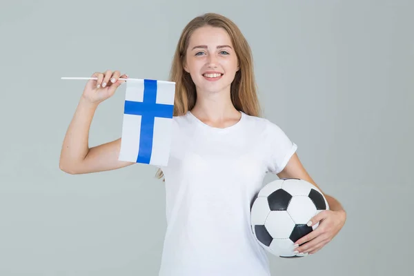 Young woman with the flag of Finland and soccer ball in her hands, looking at camera, isolated on gray background. Finnish women\'s football.