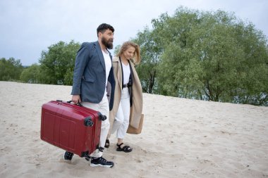 Bir çift insan, bir adam ve bir kadın, boş bir sahilde bavulla yürüyorlar. Seyahat iptal kavramı.