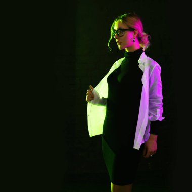 Genç bir kadın, pembe ve yeşil ışık, koyu bir arka planda.