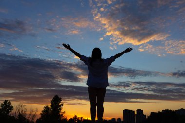 Kadın silueti. Gün batımında genç bir kadın ellerini kaldırdı. Rahatlama ve özgürlük kavramı.