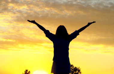 Özgürlük kavramı. Gün batımında genç bir kadının silueti ellerini kaldırdı..