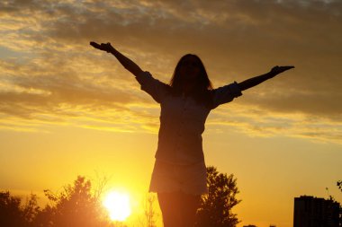 Gün batımında genç bir kadının silueti ellerini kaldırdı. Özgürlük kavramı.