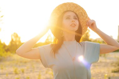 Hasır şapkalı mutlu kadın, gün batımında, yazın açık havada. Boho tarzı.