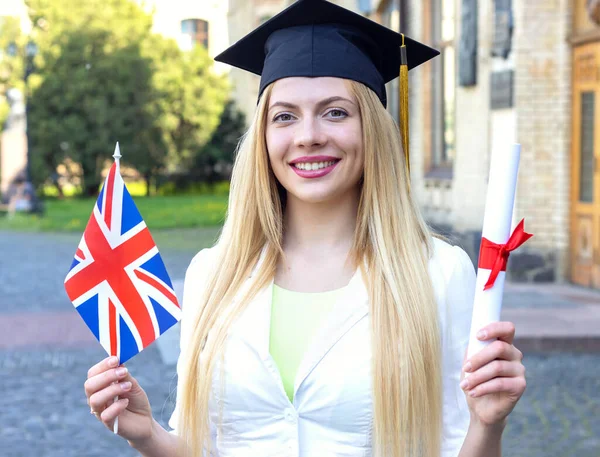 Woman student graduate with diploma and Great Britain flag. Graduation day at the university.