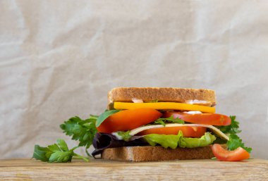 Sarı çedar peynirli lezzetli sandviç, tahıllı ekmek, yeşil roka, beyaz peynir, kırmızı domates, marul ve maydanozlu kağıt zemin üzerinde tahta bir kesim tahtası. Metin için yer.