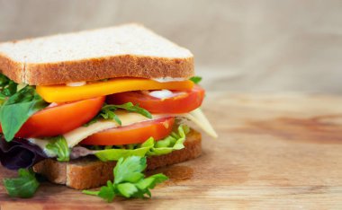 Tahta kesme tahtasında peynirli, roka, domates, marul ve maydanozlu lezzetli sandviçin manzarası. Metin için yer.