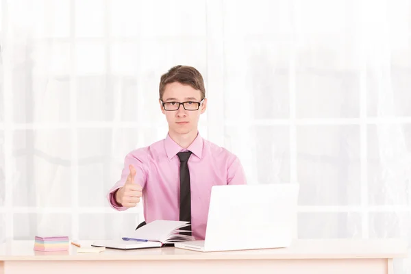 Young male student raised his thumbs up. Business man sitting at his desk, next to a laptop — Stock Photo, Image