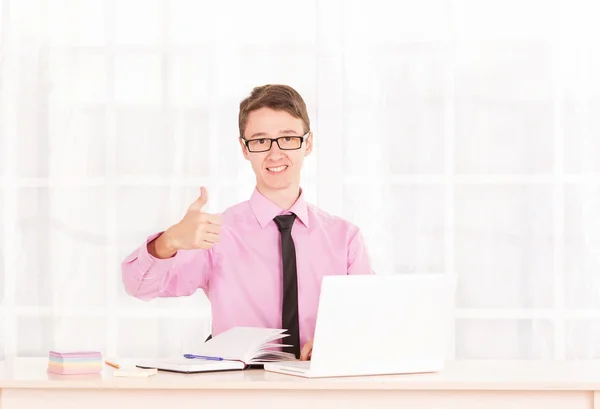 Young male student raised his thumbs up. Business man sitting at his desk, next to a laptop — Stock Photo, Image