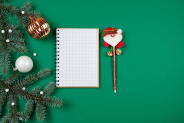 Yılbaşı dekoru, hediyeler ve yeni yıl dileklerini yazmak için bir defter ve yeşil arka planda bir kalem Noel Baba..