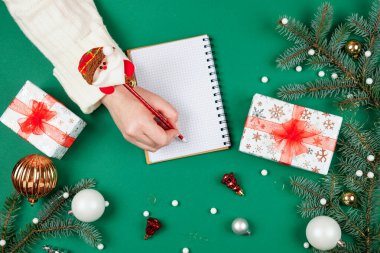 Noel dilek listesi. Noel Baba 'ya mektup yazan üst düzey düz dizayn kadın elleri. Kış tatiline ve yeni yıla hazırlanıyorum. Mevsimlik dekorasyonlu şenlikli yeşil arka plan.
