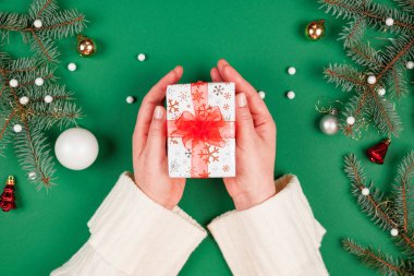Kadının elleri kırmızı kurdeleli güzel bir Noel hediyesi veriyor. Yeşil zemin ve ışıl ışıl tatil süsleri. Yeni yıl hediyeleri. Üstten bakan ilk kişi.