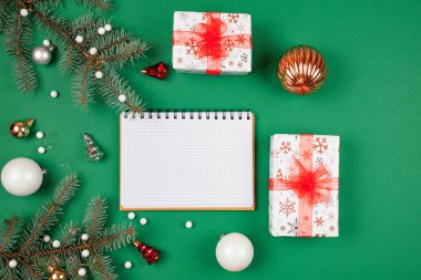 Yeni yıl hedefleri ve iş motivasyonu belirleniyor. Not defteri ve kalem, noel hediyelerinin yanında. Fotokopi alanı olan yeşil bir arka planda. Noel Baba 'ya mektup ve alışveriş listesi. Tatil planlaması.