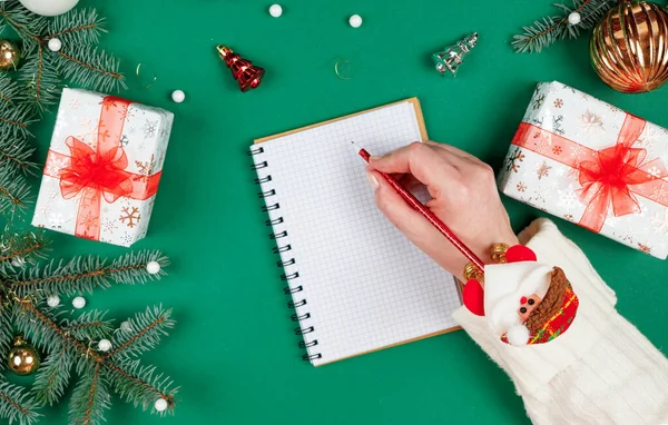 Noel dilek listesi. Noel Baba 'ya mektup yazan üst düzey düz dizayn kadın elleri. Kış tatiline ve yeni yıla hazırlanıyorum. Mevsimlik dekorasyonlu şenlikli yeşil arka plan.