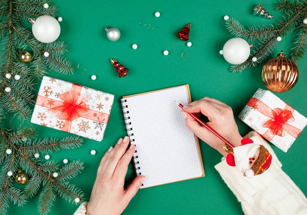 Noel dilek listesi. Noel Baba 'ya mektup yazan üst düzey düz dizayn kadın elleri. Kış tatiline ve yeni yıla hazırlanıyorum. Mevsimlik dekorasyonlu şenlikli yeşil arka plan.