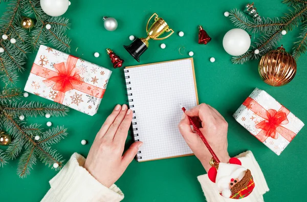 Noel dilek listesi. Noel Baba 'ya mektup yazan üst düzey düz dizayn kadın elleri. Mevsimlik dekorasyonlu yeşil bir arka plan. Kış tatiline hazırlanıyor Noel ve Yeni Yıl.