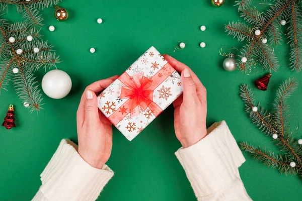 Kadının elleri kırmızı kurdeleli güzel bir Noel hediyesi veriyor. Yeşil zemin ve ışıl ışıl tatil süsleri. Yeni yıl hediyeleri. Üstten bakan ilk kişi.