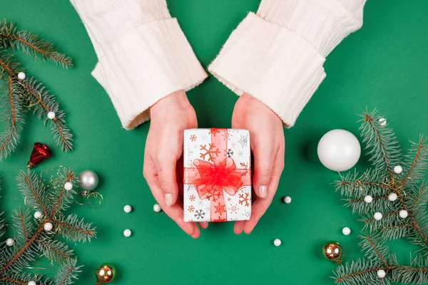 Parlak kırmızı kurdeleli bir Noel hediyesi ve kadının el ele tutuşması. Bayram hediyesi alışverişi. Yeni yıl hediyelerini yeşil arka planda süslerle karşılamak. Üstten bakan ilk kişi