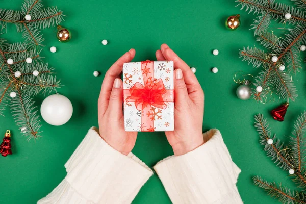Kadının elleri kırmızı kurdeleli güzel bir Noel hediyesi veriyor. Yeşil zemin ve ışıl ışıl tatil süsleri. Yeni yıl hediyeleri. Üstten bakan ilk kişi.