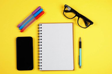 Sarı arka planda açık bir defter, renkli kalemler, gözlükler ve akıllı telefon. İş planlama, eğitim ve yaratıcı bloglar için çalışma alanı yatıyordu. Temiz model..