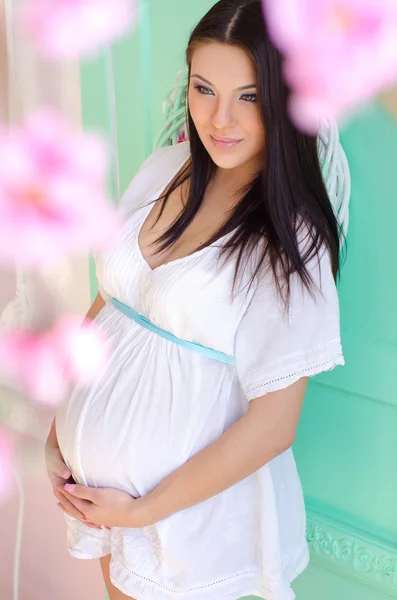 Mooie zwangere vrouw in een witte jurk op een turkooizen achtergrond — Stockfoto
