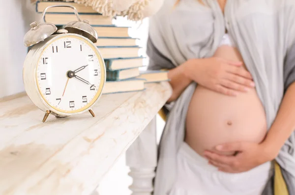 Zwangere vrouw haar buik knuffelen op de achtergrond van een wekker — Stockfoto