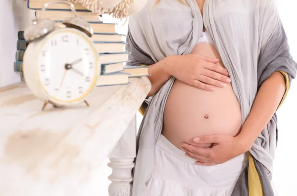 Schwangere umarmt ihren Bauch auf dem Hintergrund eines Weckers — Stockfoto