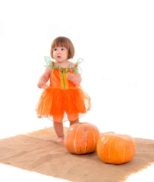 Kleines Mädchen in orangefarbenem Kostüm mit Kürbissen — Stockfoto