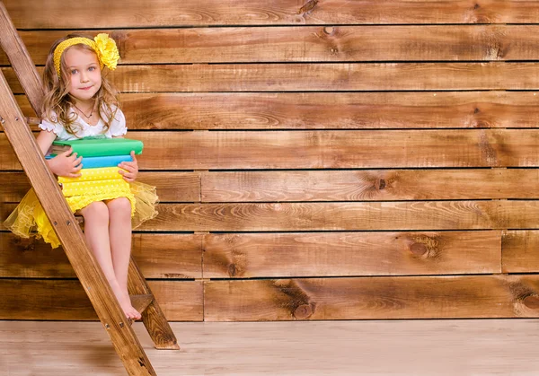 Little girl with stack of books sitting on ladder — Stock Photo, Image