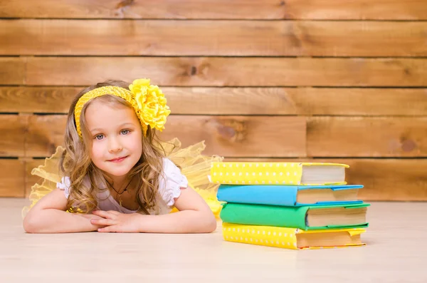 Little girl with wreath lying near stack of books — Stock Photo, Image