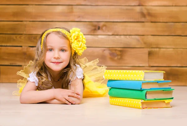 Little girl with wreath lying near stack of books — Stock Photo, Image