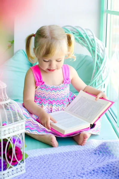 Pouco bonito menina leitura livro perto da janela — Fotografia de Stock