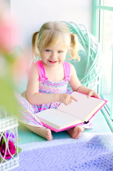 Niña divertida leyendo libro cerca de la ventana —  Fotos de Stock