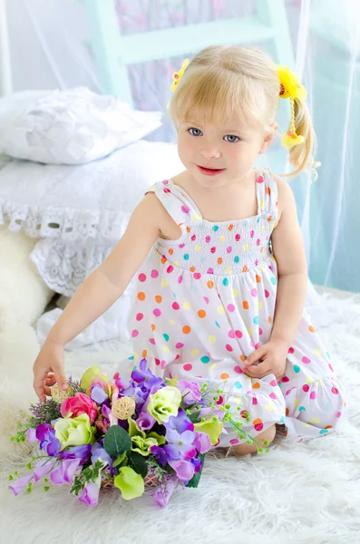 Little girl sitting on bed with bouquet of flowers — Stock Photo, Image