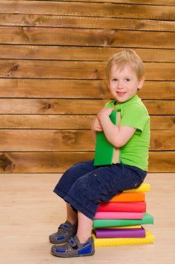 renkli kitap yığını üzerinde oturan küçük çocuk