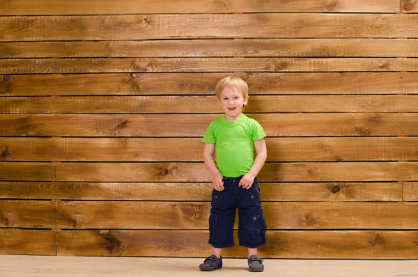 Niño pequeño con camisa verde cerca de la pared de madera — Foto de Stock