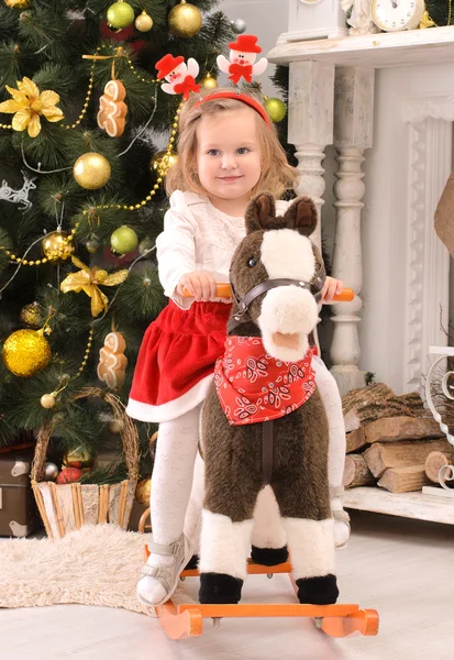 Little girl on toy horse in christmas interior — Stock Photo, Image