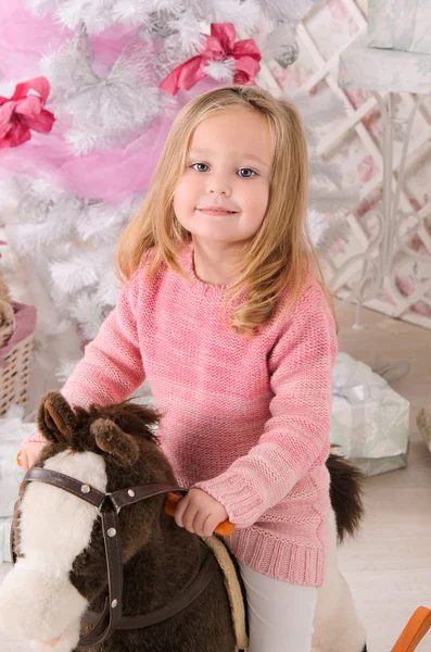 Little girl on toy horse in christmas interior — Stock Photo, Image