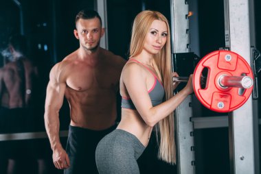 Spor salonunda ağırlık adamla egzersiz genç çift kişisel antrenör gibi görünüyor