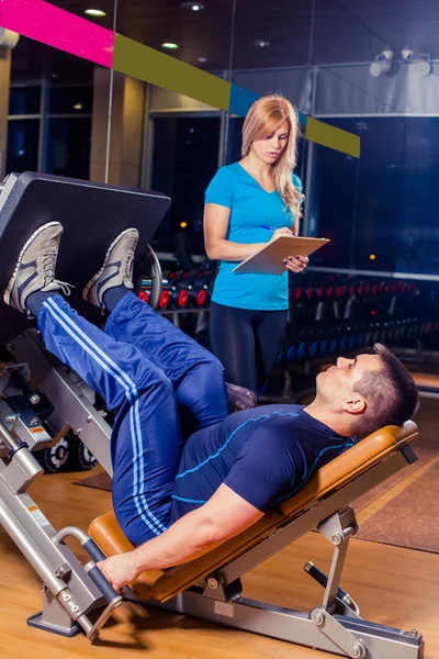 Entrenador personal que ayuda a un hombre a ejercitarse en la máquina de prensa de piernas en el gimnasio — Foto de Stock