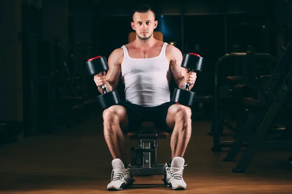 Esporte, musculação, levantamento de peso, estilo de vida e conceito de pessoas - jovem com halteres flexionando músculos no ginásio — Fotografia de Stock