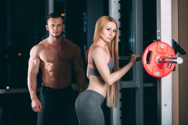Spor salonunda ağırlık adamla egzersiz genç çift kişisel antrenör gibi görünüyor