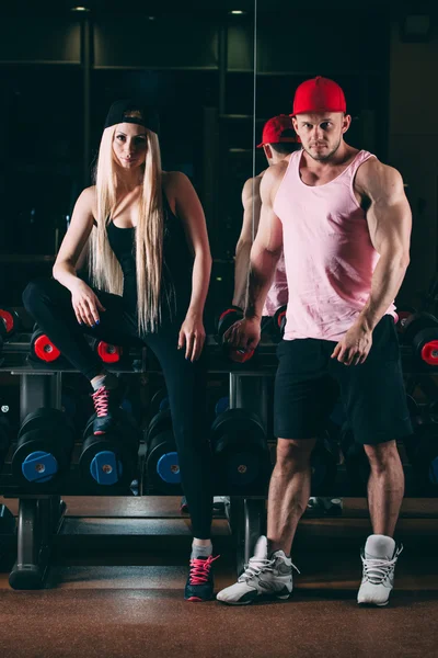 sport, bodybuilding, weightlifting, lifestyle and people concept - Young beautiful couple in stylish clothes sitting a gym near the dumbbells
