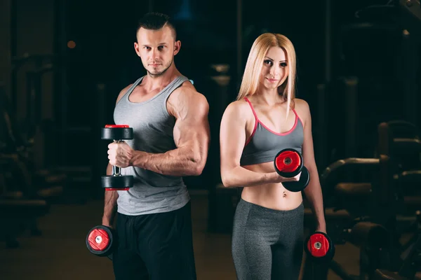 Hermosa joven deportivo sexy pareja mostrando músculo y entrenamiento en gimnasio dumbbell —  Fotos de Stock