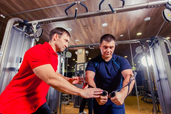 Entrenador personal que ayuda a los hombres a ejercitarse en la sala de pesas en el gimnasio —  Fotos de Stock
