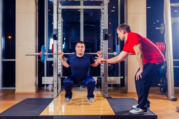 Deporte, fitness, trabajo en equipo, culturismo concepto de personas - hombre y entrenador personal con los músculos de flexión de la barra en el gimnasio — Foto de Stock