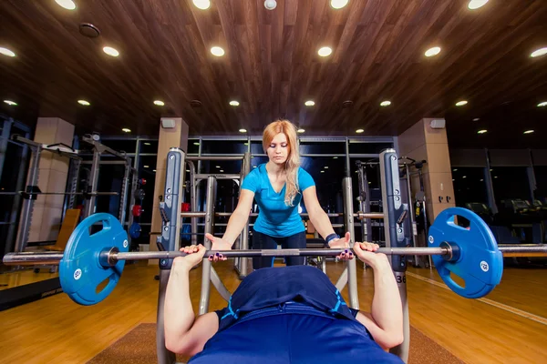 Personal trainer helping  men lift a barbell while working out in  gym — Stock Photo, Image